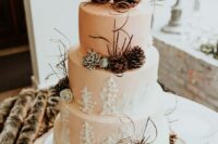 a blush wedding cake with painted fir trees, pinecones, twigs and pinecone marrying couple on top is a fun idea