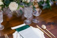 a chic winter wedding table setting with emerald napkins, gold cutlery, chic glasses and lush white bloom and greenery centerpieces