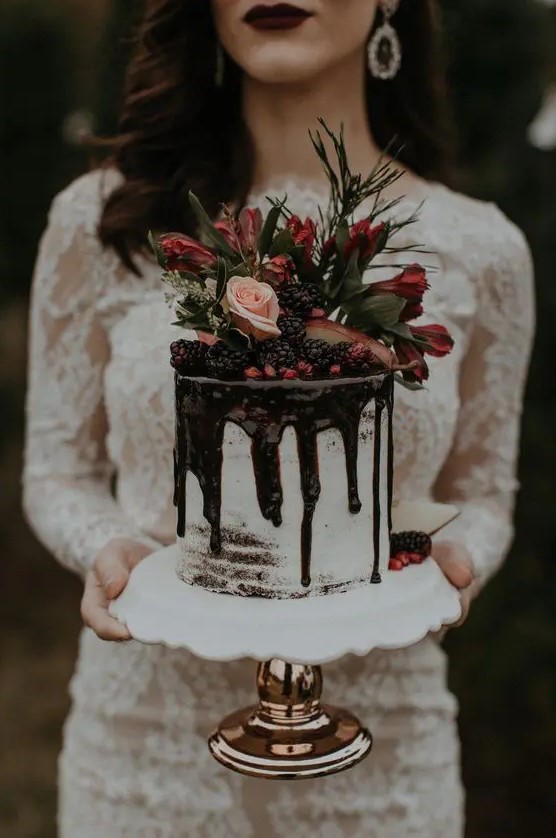 a mini wedding cake with chocolate drip, blackberries, pomegranate seeds, greenery, blush and red blooms