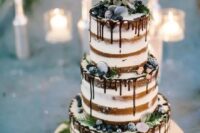 a naked wedding cake with chocolate drip, sugared berries, greenery and ferns is a stylish option for a winter wedding