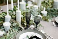 a natural winter wedding table in grey and greens, concrete candleholders, black glasses and grey plates and black ribbons