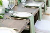 a natural winter wedding table with a greenery runner, candles, green napkins, gold cutlery
