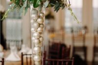 a neutral holiday centerpiece of metallic ornaments in a tall vase, foliage and white blooms plus branches