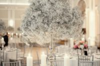 a pure white winter wedding centerpiece of a tall silver vase with white blooms and silver candleholders with candles