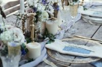 a rough winter wedding table with an uncovered table, pillar candles, white and purple blooms, twigs and refined glasses