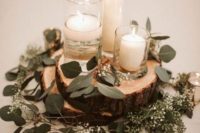 a simple and cozy rustic winter wedding centerpiece of wood slices, eucalyptus, candles in candleholders
