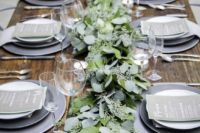 a simple and neutral winter wedding tablescape with grey plates, a eucalyptus runner, grey menus and elegant cutlery