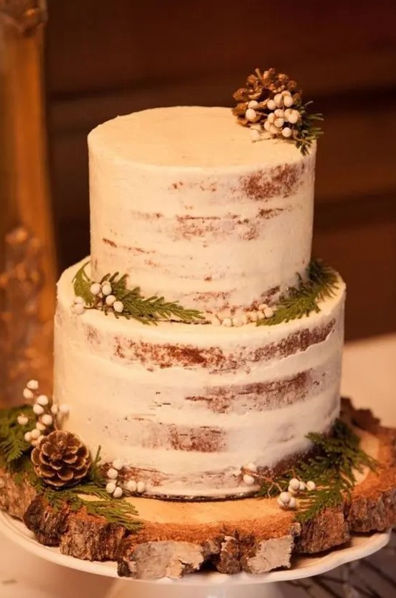 a simple semi naked wedding cake topped with pinecones, ferns and berries for a rustic winter wedding