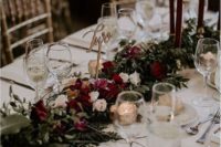 a stylish and lush winter wedding table with a refined floral and greeneryrunner, burgundy candles, mercury glass and an elegant table number