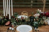 a stylish winter wedding table with a lush greenery, suculent, burgundy blooms runner, candles and pomegranates