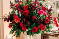 a super bright holiday wedding centerpiece with red and fuchsia blooms, foliage and berries