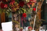 a whimsy winter wedding centerpiece of a tall vase with moss and pinecones and moody blooms for a cool look