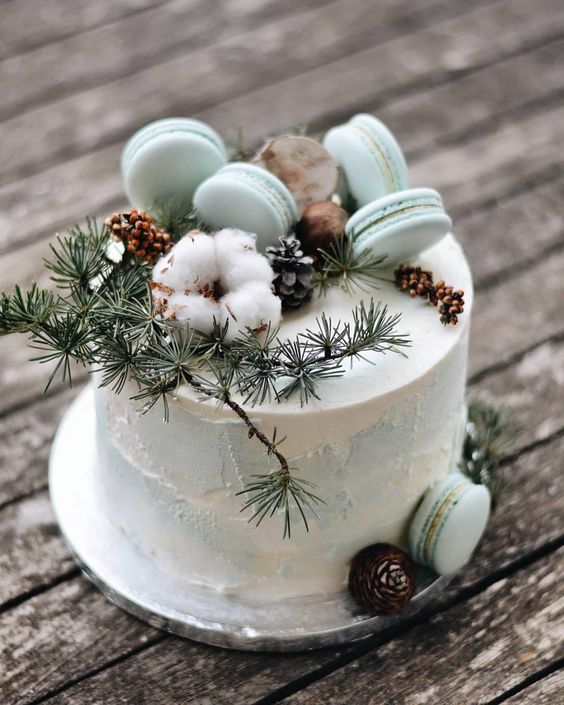a white and blue textural wedding cake with mint green macarons on top, cotton, pinecones and evergreens is a chic idea for a winter wedding