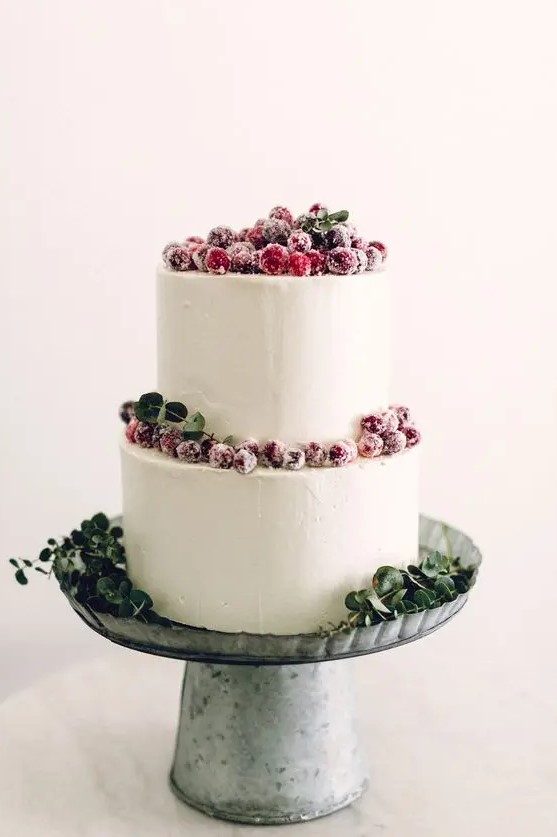 a white buttercream wedding cake decorated with greenery and sugared berries is a stylish idea