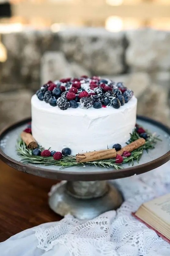 a white textural buttercream wedding cake topped with sugared berries, with cinnamon and rosemary is a cool rustic idea