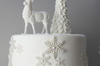 a white wedding cake decorated with sugar snowflakes, topped with a Christmas tree and a deer is a chic and stylish idea