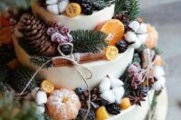 a white wedding cake topped with a whole number of stuff – citrus, berries, pinecones, cinnamon bark, cotton and evergreens