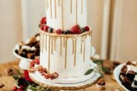 a white wedding cake with gold drip, sugared berries, a rose and eucalyptus for a chic winter wedding