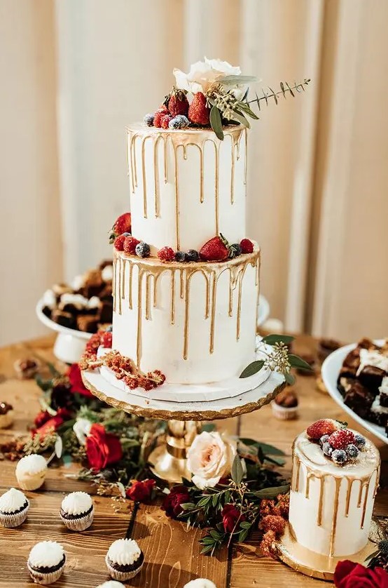 a white wedding cake with gold drip, sugared berries, a rose and eucalyptus for a chic winter wedding