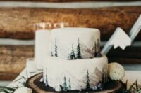 a white wedding cake with painted mountains and fir trees is a great idea for a winter mountain wedding