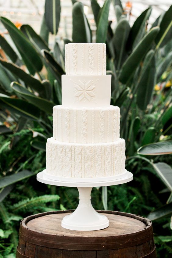 a white wedding cake with tiers decorated with patterns inspired by sweaters is a cozy and pretty solution for a winter wedding