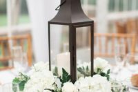 a winter wedding centerpiece of white blooms and a candle lantern plus ferns around