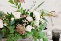 an organic winter wedding centerpiece of greenery, white and burgundy blooms and twigs