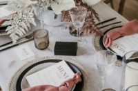 an unusual winter wedding tablescape with pink napkins, black plaes and a white centerpiece with blooms and foliage