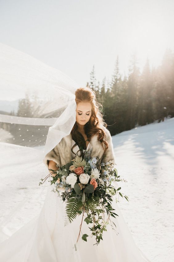a beautiful winter bridal look with a neutral faux fur cover up and an embellished long veil is glam and chic