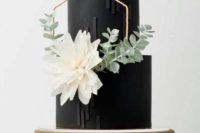 a black and white wedding cake decorated with stripes, a hexagon, a white bloom and some greenery