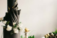 a black wedding cake with much texture and a gold rim, white blooms and greenery