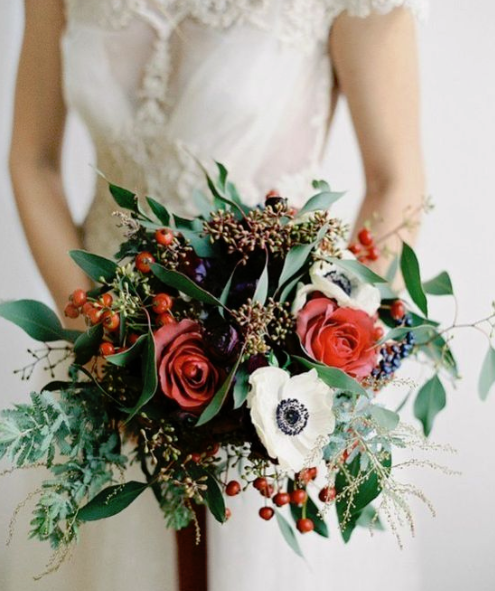 a bright winter wedding bouquet of red blooms and berries, white anemones and much greenery and foliage