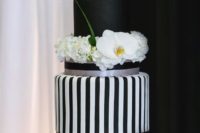 a chic black and white wedding cake with striped and a solid tier, white blooms and greenery for a whimsy touch