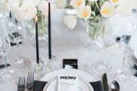 a chic modern black and white wedding tablescape with a black napkin, candles and dark cutlery plus lush white blooms