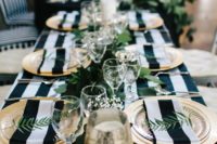 a chic modern tablescape with a striped tablecloth and napkins, much greenery and gilded touches for a touch of lux