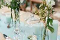 a chic wedding tablescape with a mint table runner and mint pillar candles, neutral blooms and cutlery