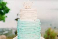 a coastal wedding cake in white and minty blue with ruffled tiers and a coral on top