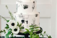 a creative black and white brushstroke wedding cake decorated with greenery and white anemones is very chic