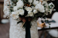 a dimensional winter wedding bouquet with white blooms, berries, grasses and greenery plus emerald ribbons