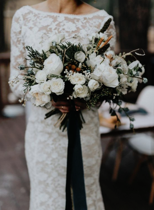a dimensional winter wedding bouquet with white blooms, berries, grasses and greenery plus emerald ribbons