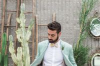 a groom wearing a mint wedding suit, a printed bow tie and suspenders looks cool and bold
