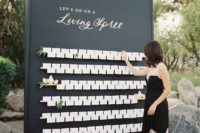 a large black seating chart with white cards and some blooms is a chic idea for a modern wedding
