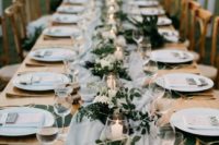 a long table spruced up with an airy grey table runner, candles in glass candle holders and lush greenery and white blooms
