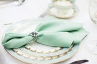a mint, white and gold plates and a mint napkin with a brooch napkin ring for a refined tablescape