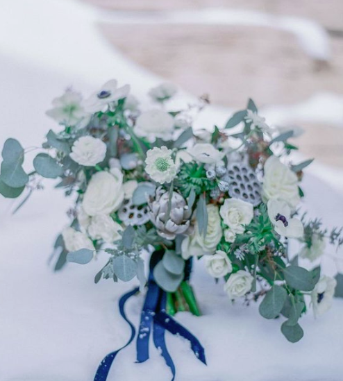 a pale winter wedding bouquet of white blooms, silver touches and lotus plus blue ribbons
