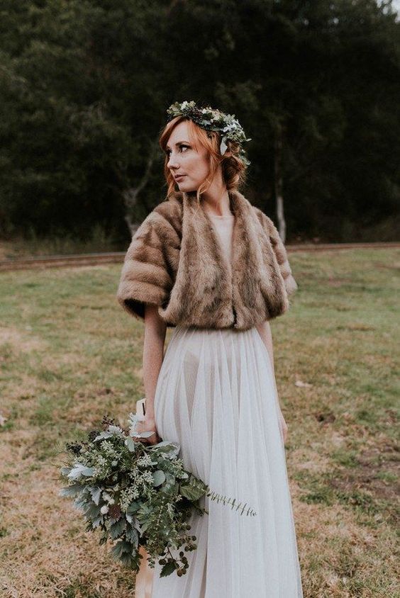 a romantic A-line wedding dress with a semi sheer skirt, a brown faux fur cover up and a greenery crown for a fall bride
