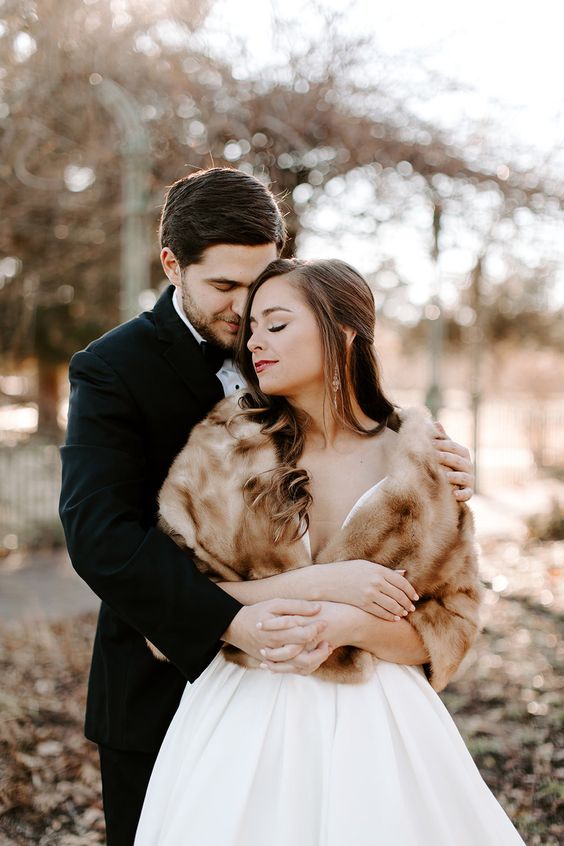 a romantic and refined winter bridal look with a plain wedding ballgown and a beige faux fur cover up plus statement earrings