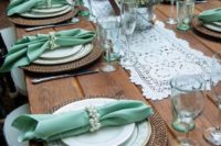a rustic wedding tablescape with an uncovered table, a doily table runner, woven chargers and mint napkins and glasses