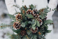 a simple and cozy winter wedding bouquet of evergreens, eucalyptus and snowy pinecones