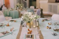 a spring wedding table with a burlap and lace table runner, mint napkins, white blooms and greenery centerpiece and candles